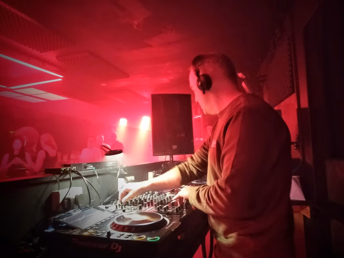 Moss B wearing headphones and mixing behind the decks at BlueBox, York, under red lighting.