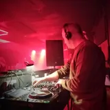 Moss B wearing headphones and mixing behind the decks at BlueBox, York, under red lighting.
