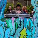 Smiley Jack wearing headphones behind the decks in a colourful outdoor RARE DJ booth.