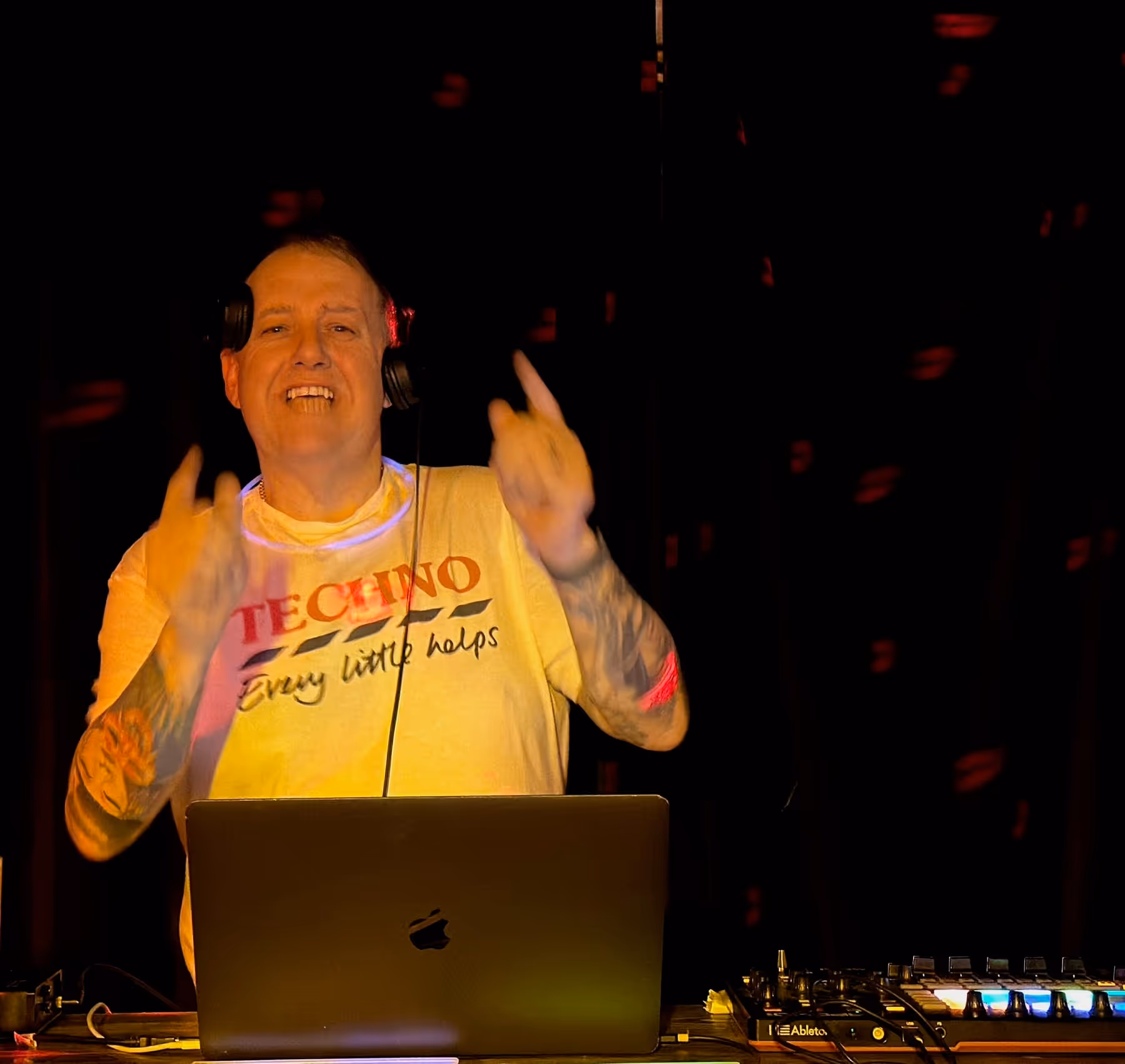 Tony T smiling behind a laptop and DJ controller in a dark booth.